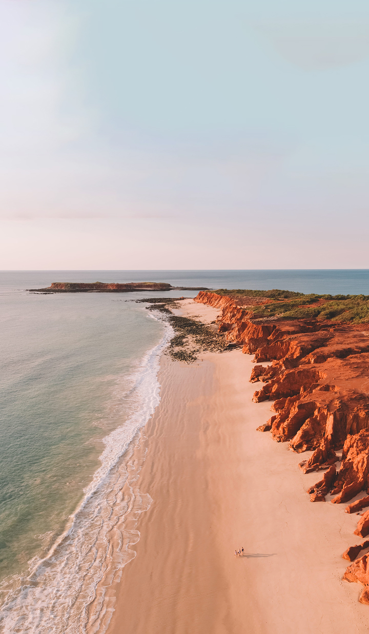 Aerial view of Cape Leveque at sunset, with red cliffs, sandy beach, and people walking along the shoreline.