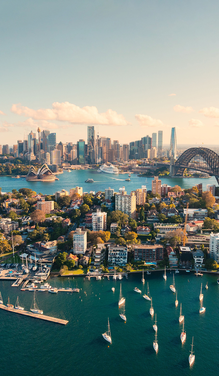 Aerial view of Sydney Harbour, boats at Kirribilli, Opera House and Harbour Bridge in warm sunlight.