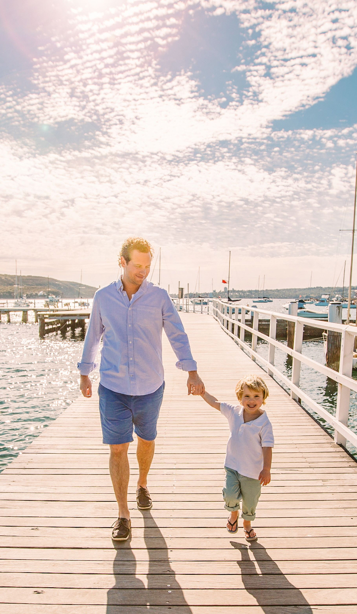 Father and son holding hands while walking along a jetty on a sunny summer day.