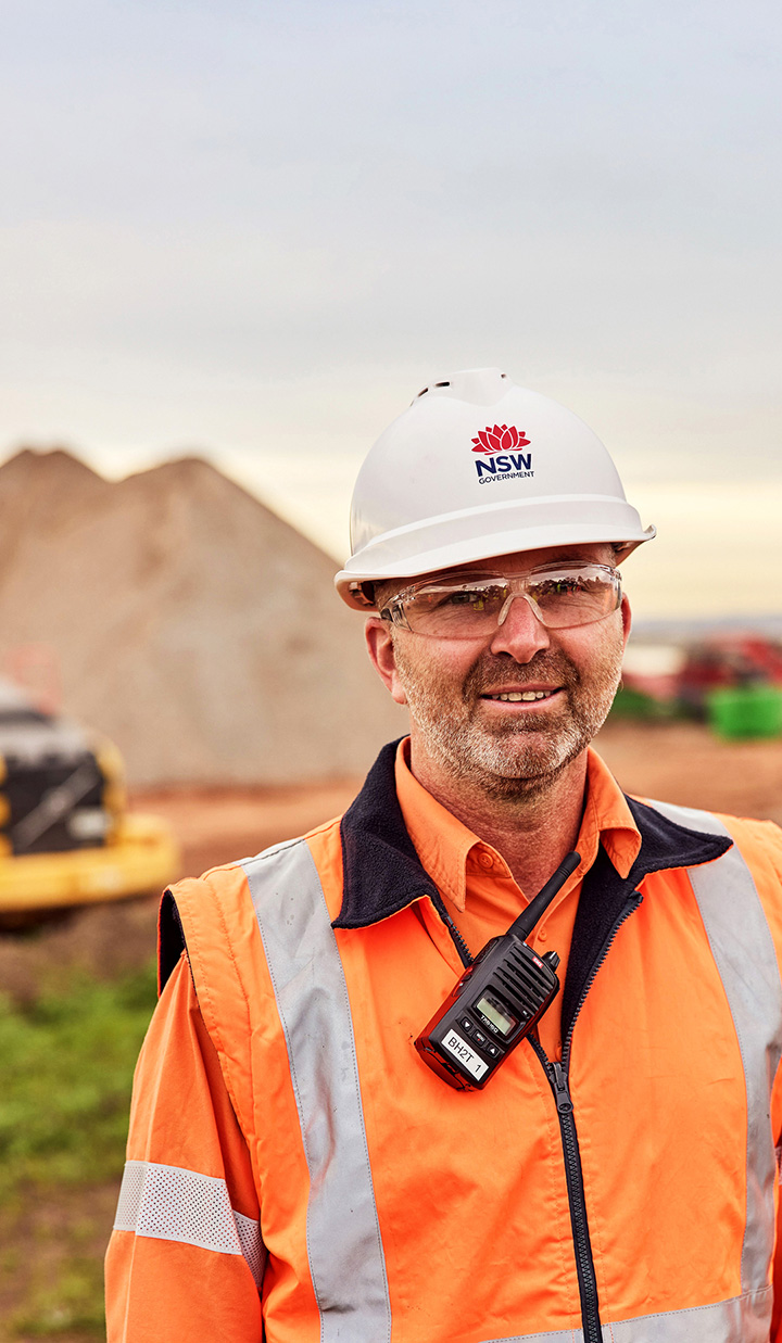 NSW worker on a construction site with a walkie talkie attached to their vest and wearing a PPE hat.