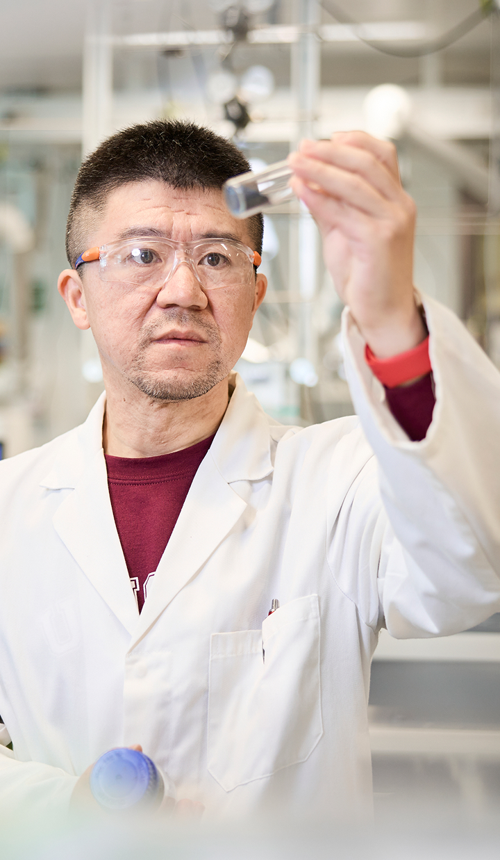 Yansong Shen holding up a scientific glass and looking at it thoughtfully