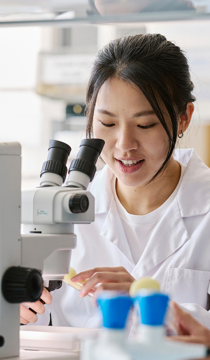 Female scientist in lab coat using microscope in laboratory.