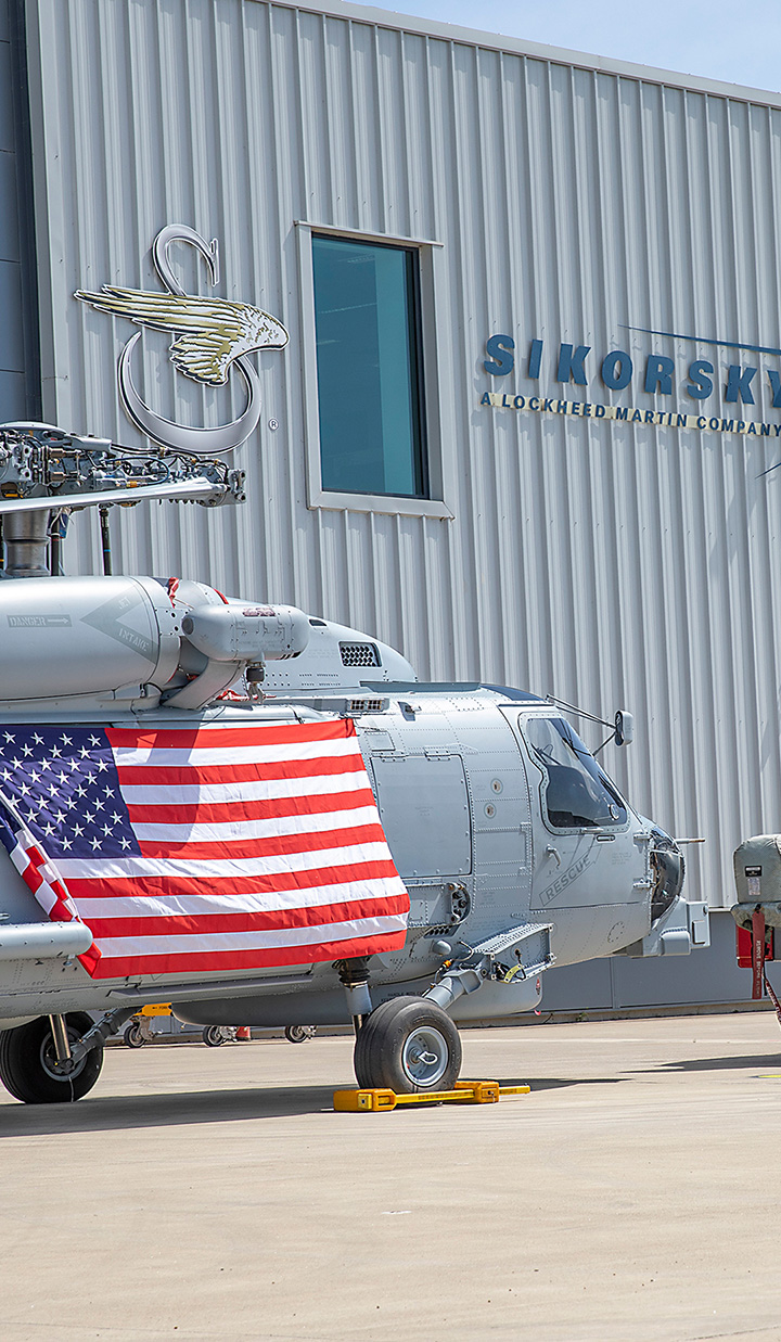 Helicopter with American flag in front of Sikorsky building.