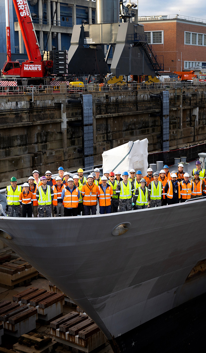 large group of workers in safety vests standing on ship