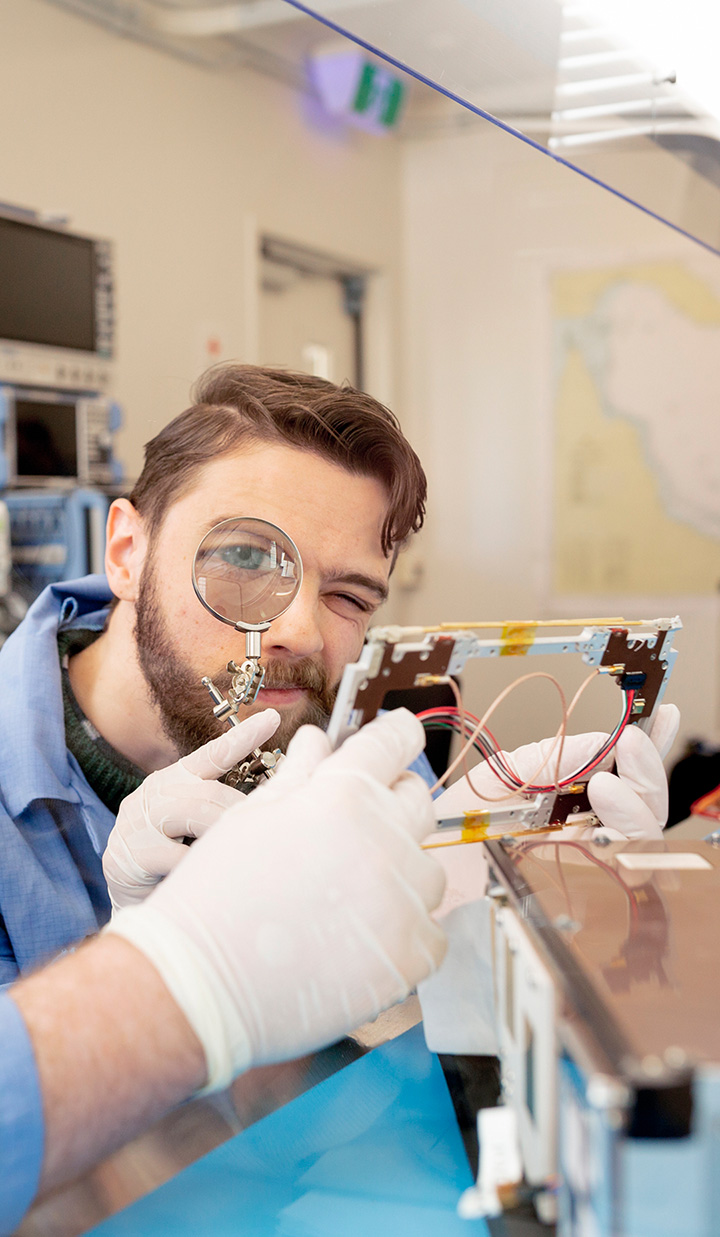man in blue lab coat inspecting electronic component with magnifier