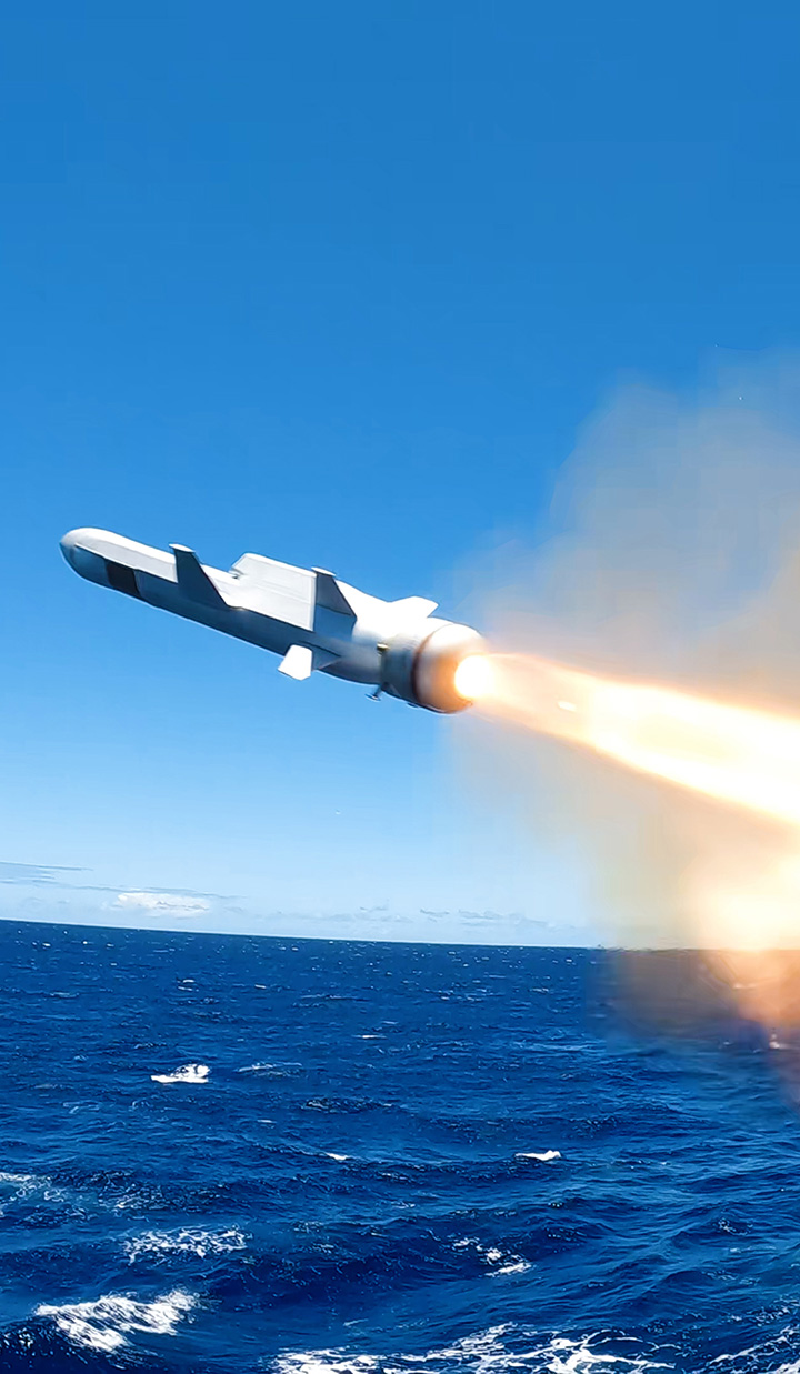 Missile launching over ocean leaving trail of fire.