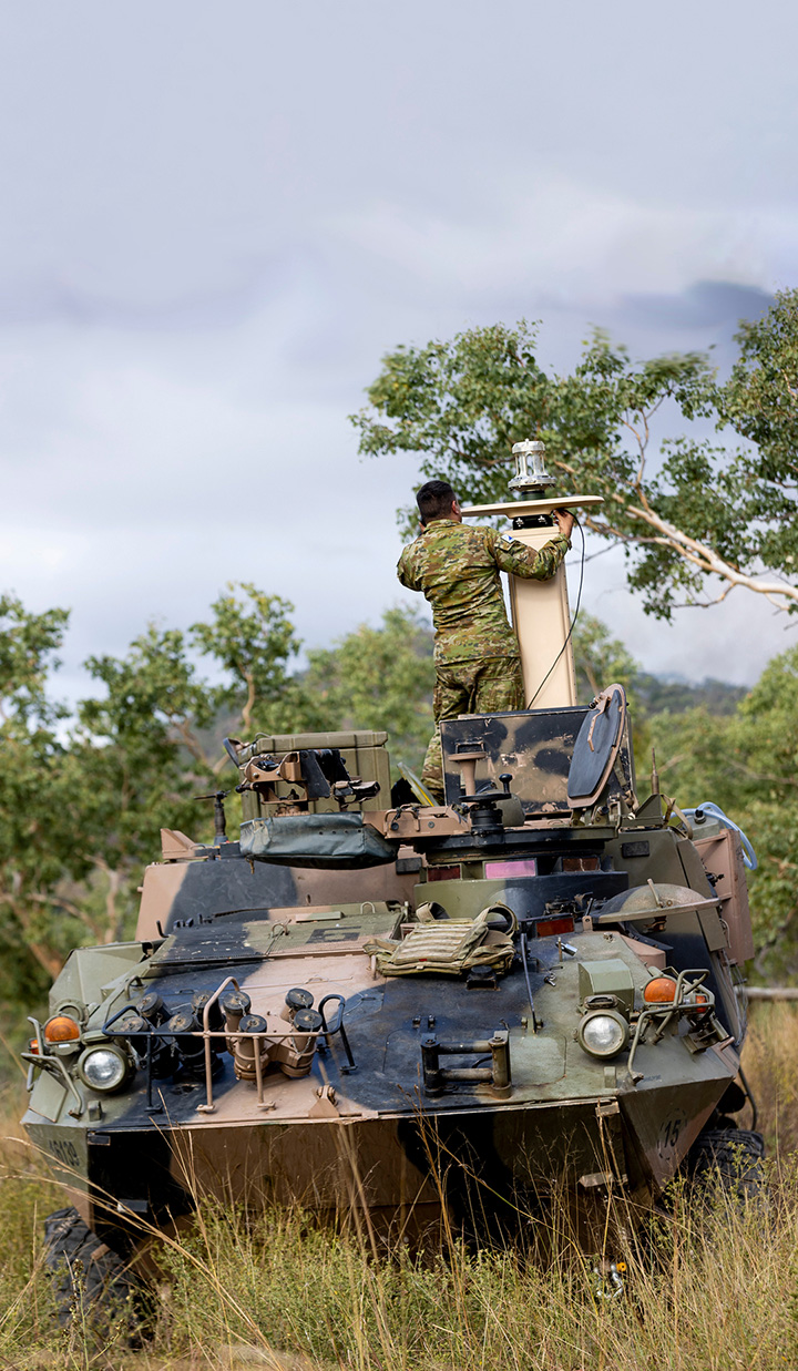 Soldier standing on armored vehicle in field.