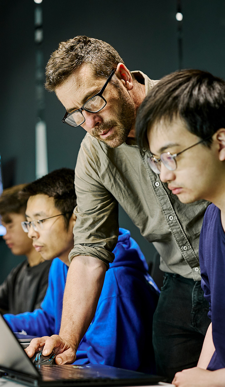 Teacher assisting students on computers in classroom.