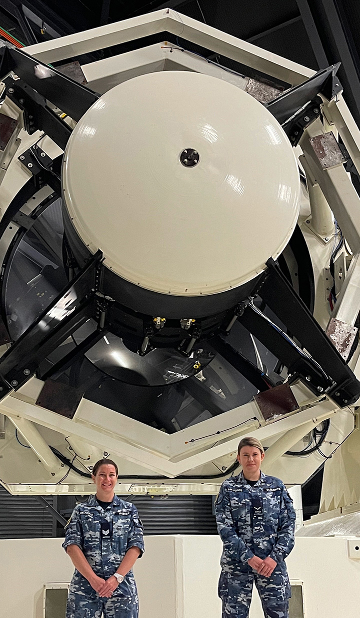Two uniformed women standing in front of large telescope.