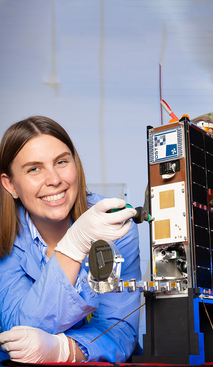 Woman smiling working on satellite component in lab.