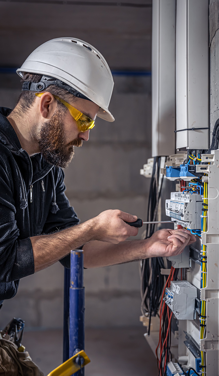 electrician-adjusting-wiring-in-electrical-panel-wearing-safety-gear