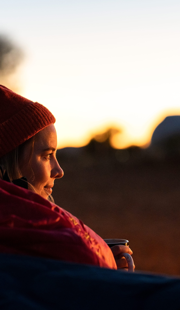 woman-sitting-outdoors-at-sunrise-holding-warm-drink