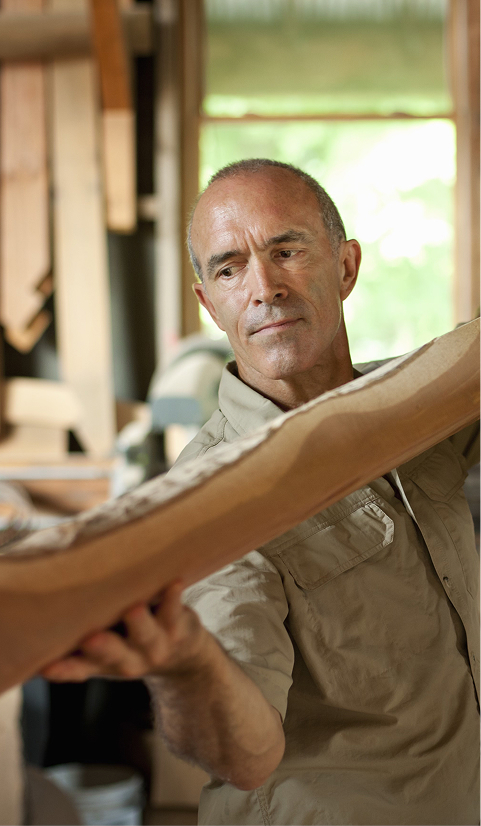 Experienced craftsperson inspecting a shaped timber piece in a workshop