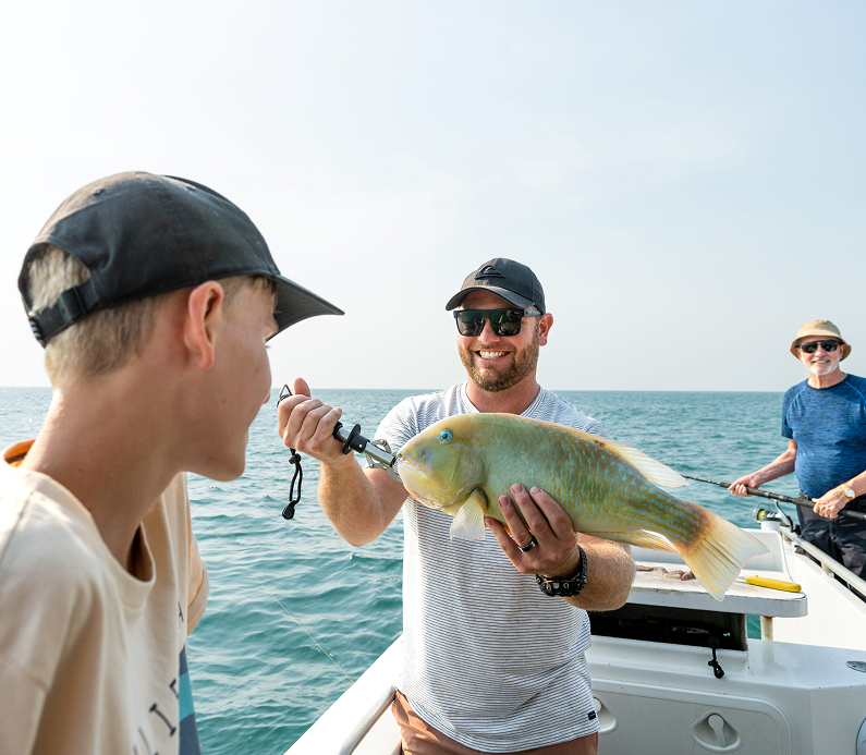 Father holds up a fresh-caught fish as family members look on in the boat