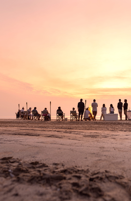 Beachside gathering with people chatting around a campfire at sunset