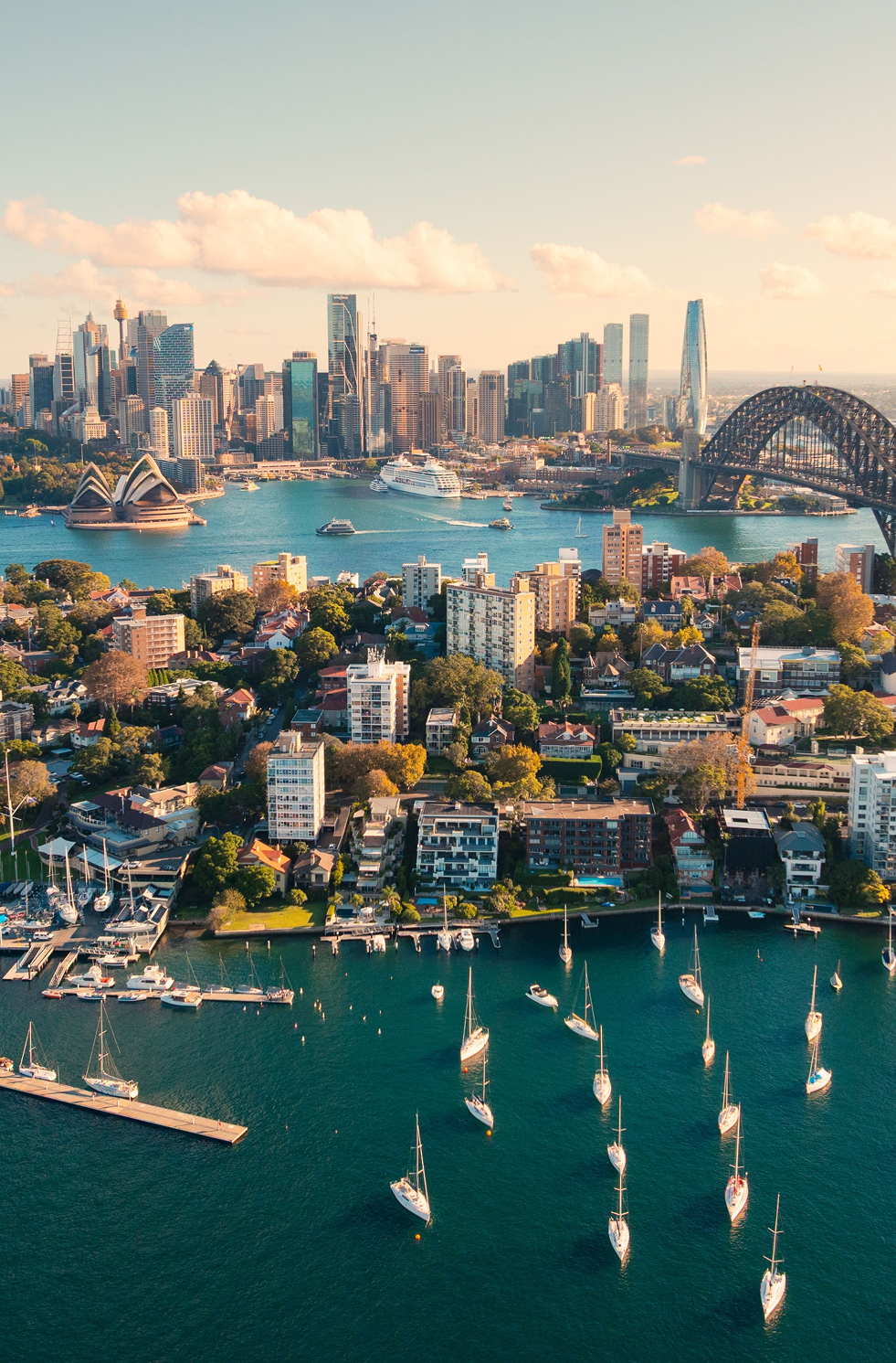 Aerial view of Sydney Harbour, boats at Kirribilli, Opera House and Harbour Bridge in warm sunlight.