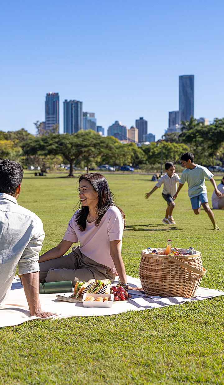 family having picnic on grass in park with city skyline in background