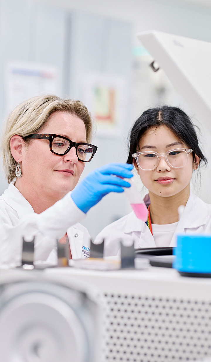 two researchers in lab coats examining vial with pink liquid