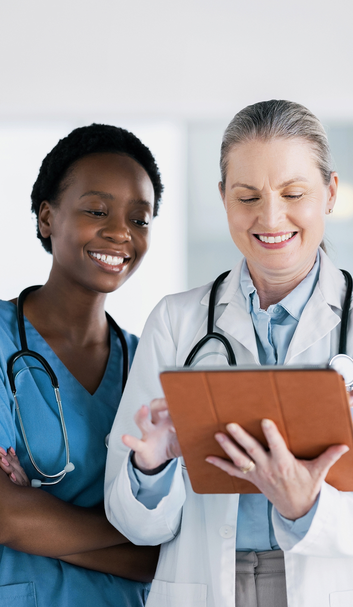 Two healthcare professionals stand together while reviewing information on a tablet device.