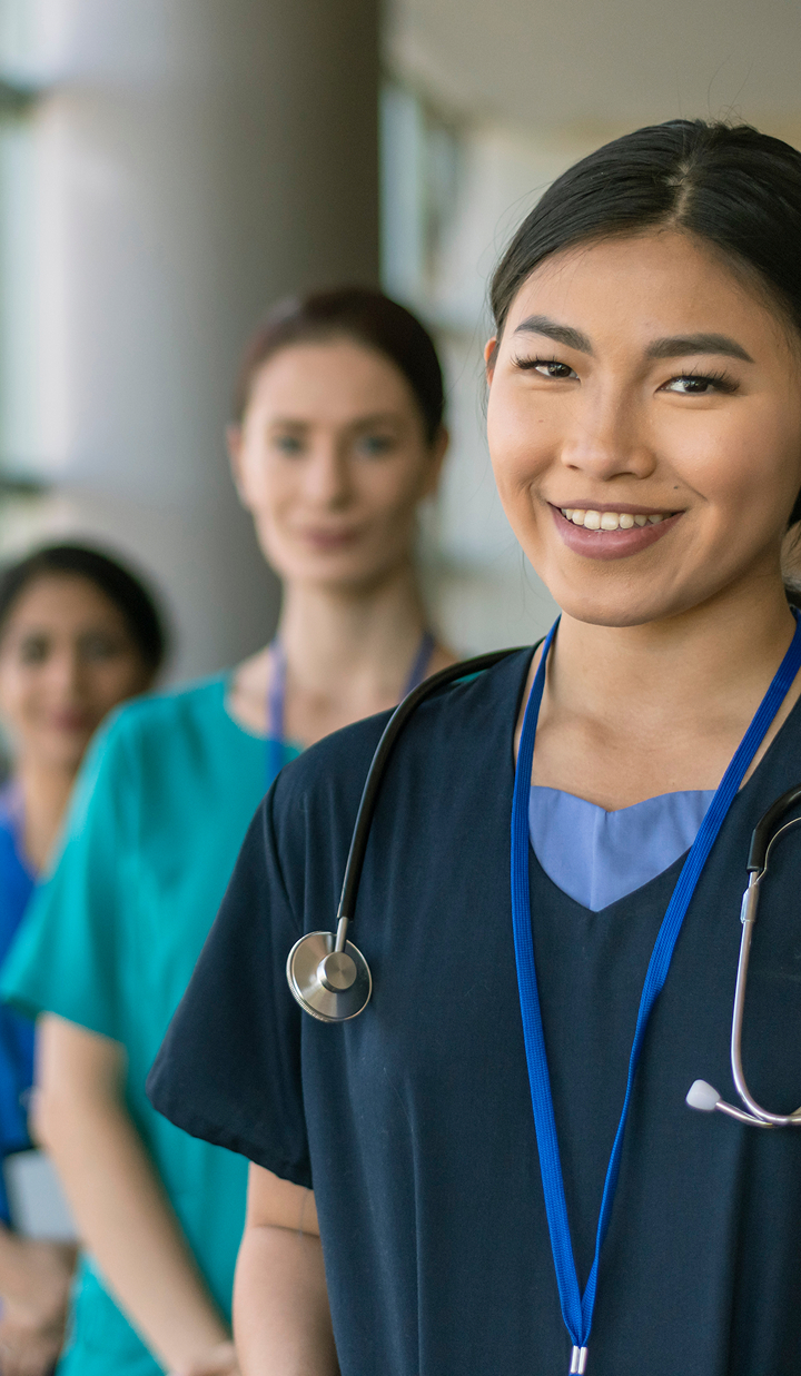 A group of healthcare professionals in scrubs stand in a line in a hospital corridor, with stethoscopes visible on their uniforms.