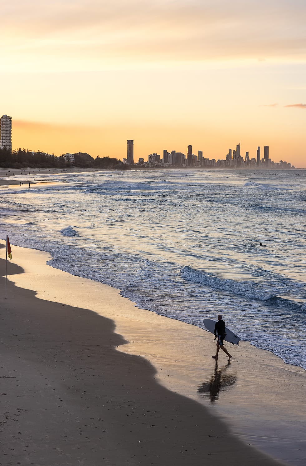 Lone surfer walking on beach at sunset