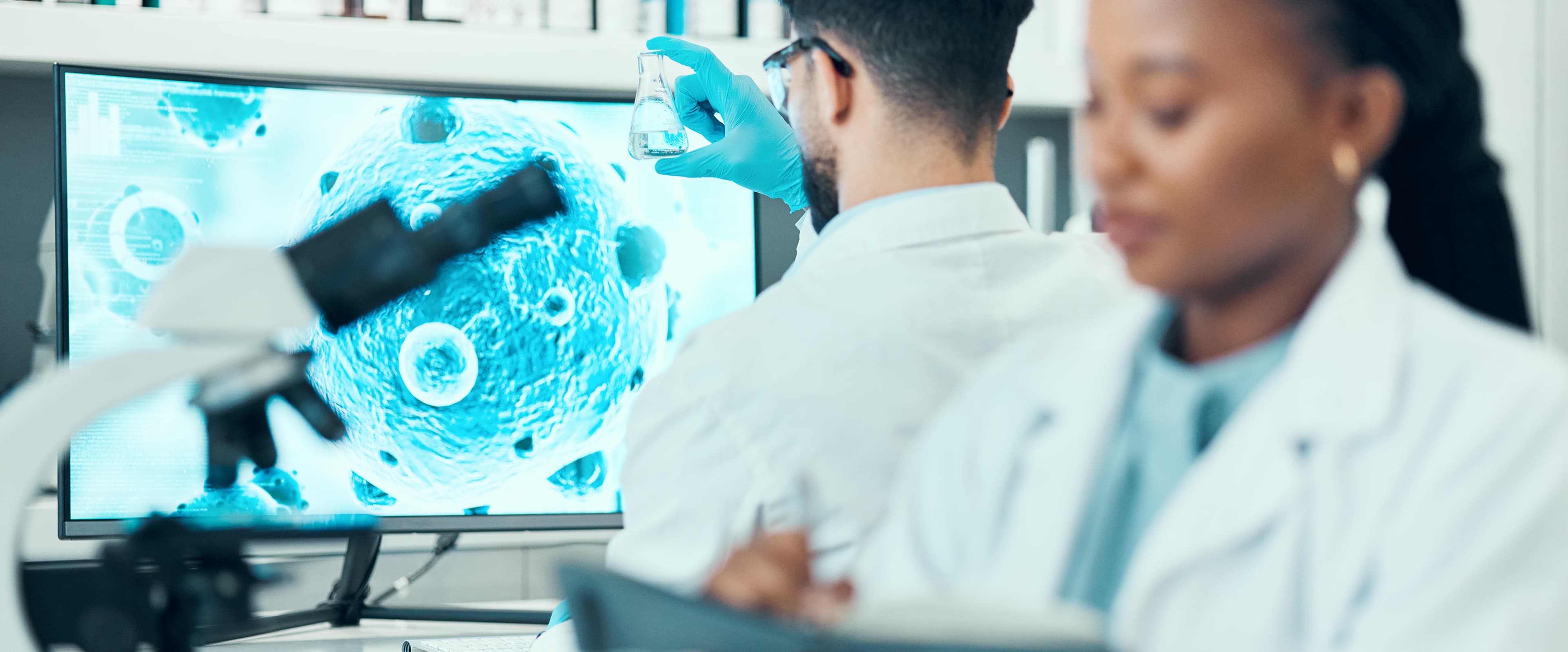 Scientists in a laboratory examine a flask and tablet beside a microscope image of cells displayed on a screeneco-friendly plastic innovation