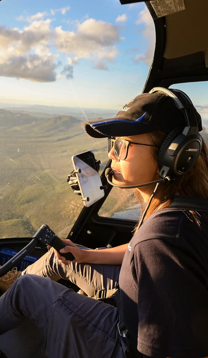 Female pilot flying a helicopter above Australia’s bushland.