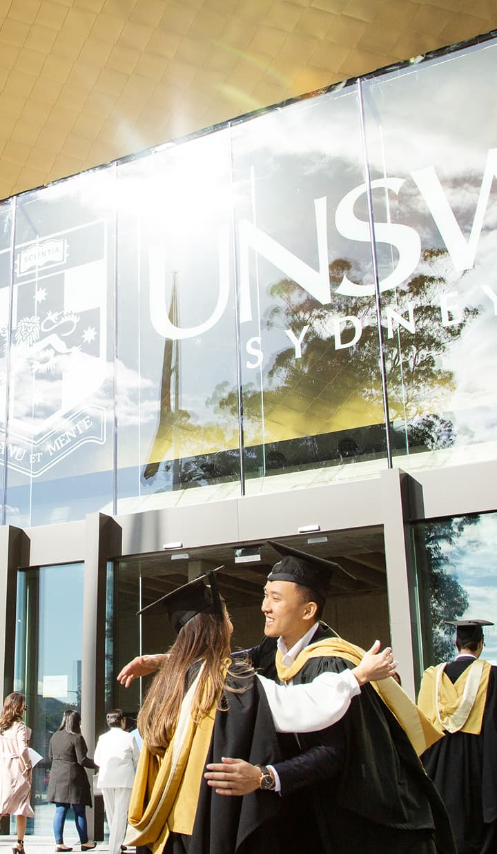 Sydney Uni students in graduation gowns hugging to celebrate