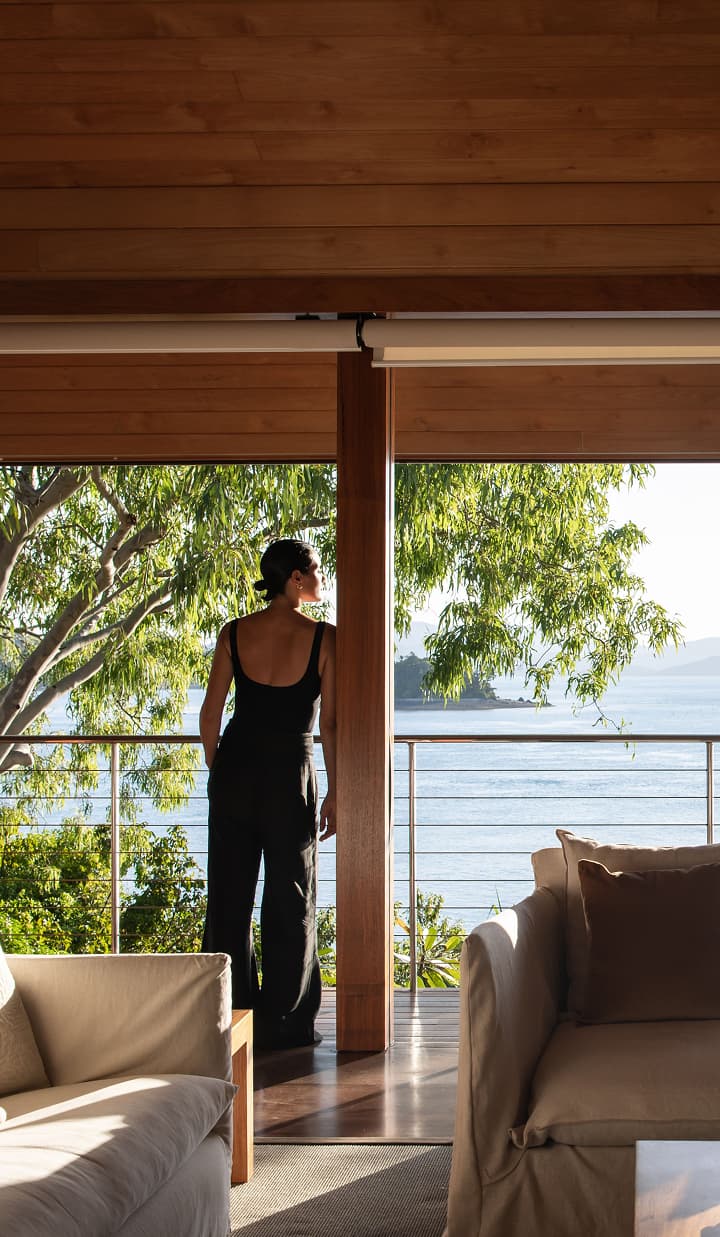 Woman enjoys a peaceful moment at home, gazing out to a balcony with ocean and bushland views.