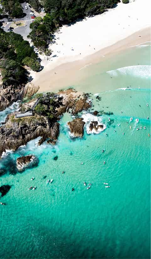 Aerial view of a sandy beach with turquoise water, rocky outcrops, and swimmers in the ocean