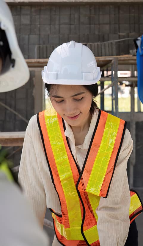 Female construction worker wearing a hard hat and high-visibility vest reviewing building plans at an active worksite