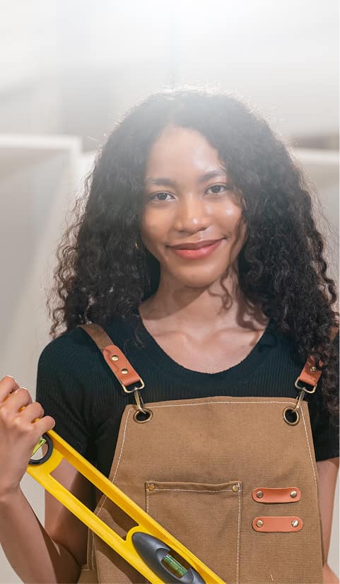 Female tradesperson wearing overalls and holding a spirit level inside a workshop or building interior