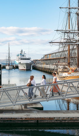 People walking along the Hobart waterfront near historic ships and modern vessels