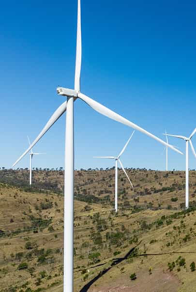 A landscape of grassy hills with multiple large white wind turbines under a clear blue sky
