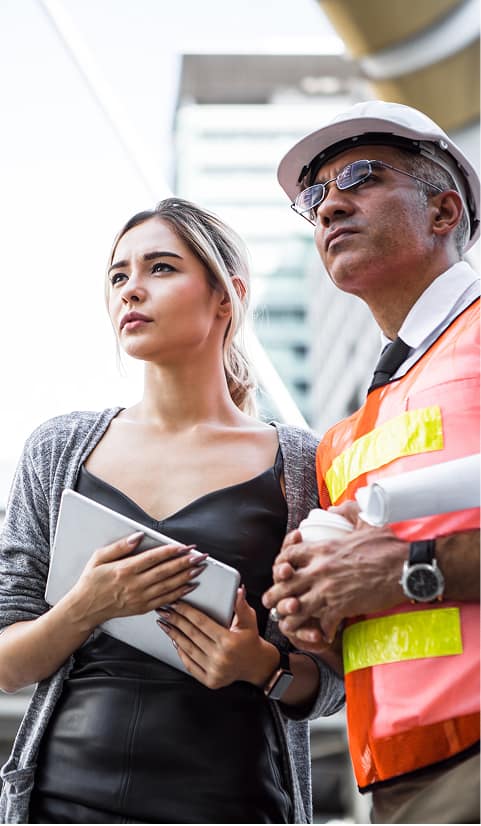 Two construction professionals in safety gear reviewing a building site with plans