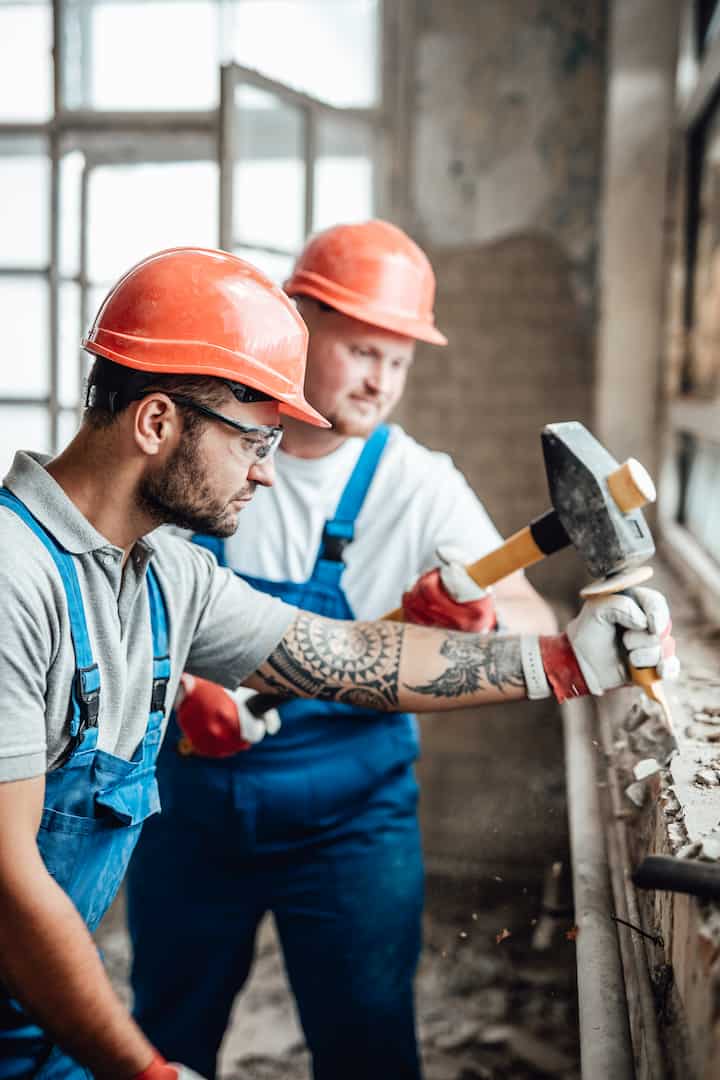 A couple of builders working together with a sledgehammer