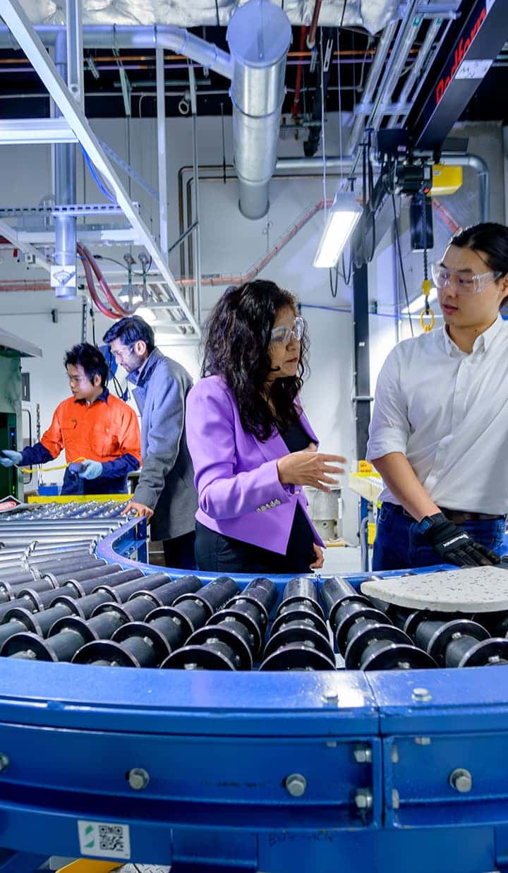 A group of people in a factory or lab setting working near a conveyor belt