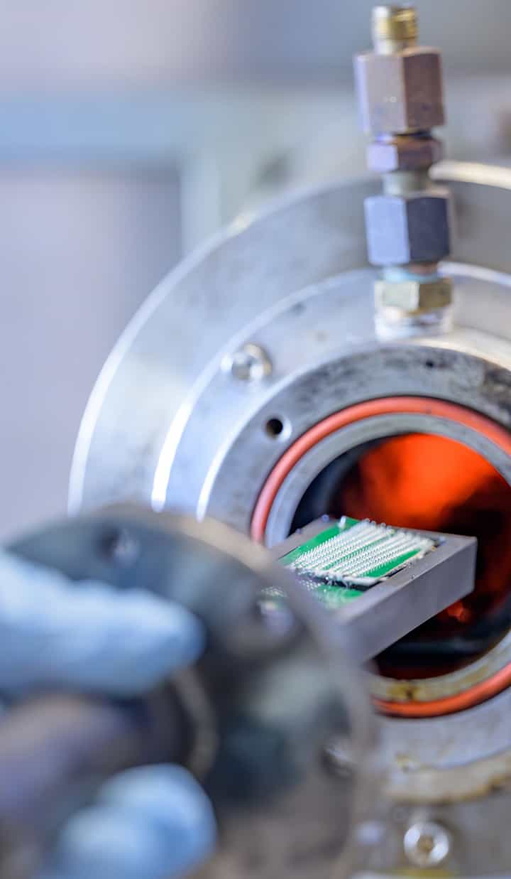 A person inserting a chip or circuit board into a furnace-like machine.