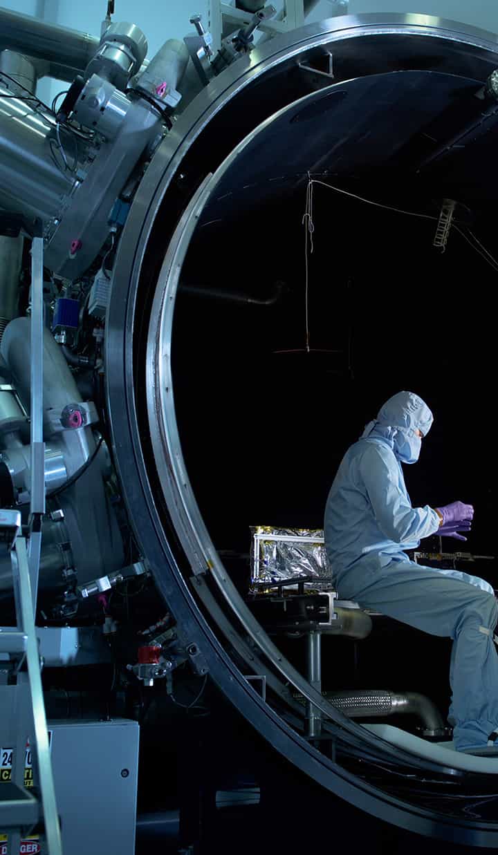 A person wearing a lab vest working inside a large steel tube, appearing to install or fix big equipment.
