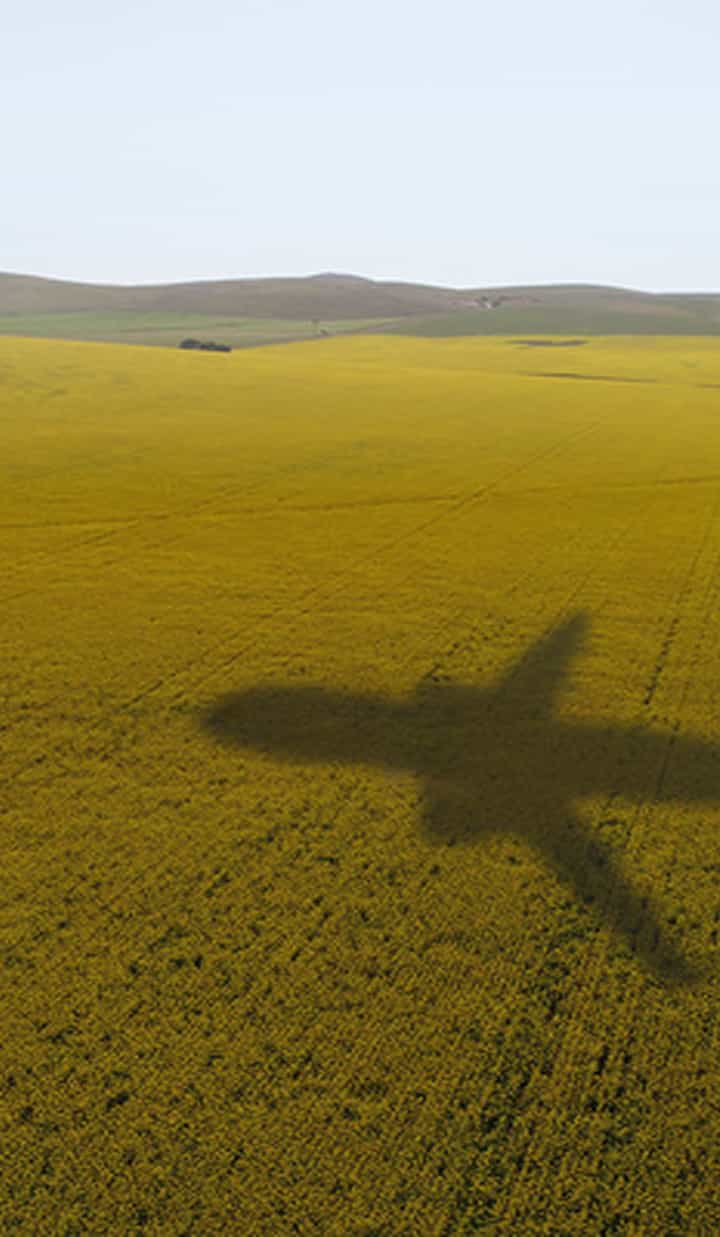 The shadow of an airplane cast over a wide yellow field with distant hills
