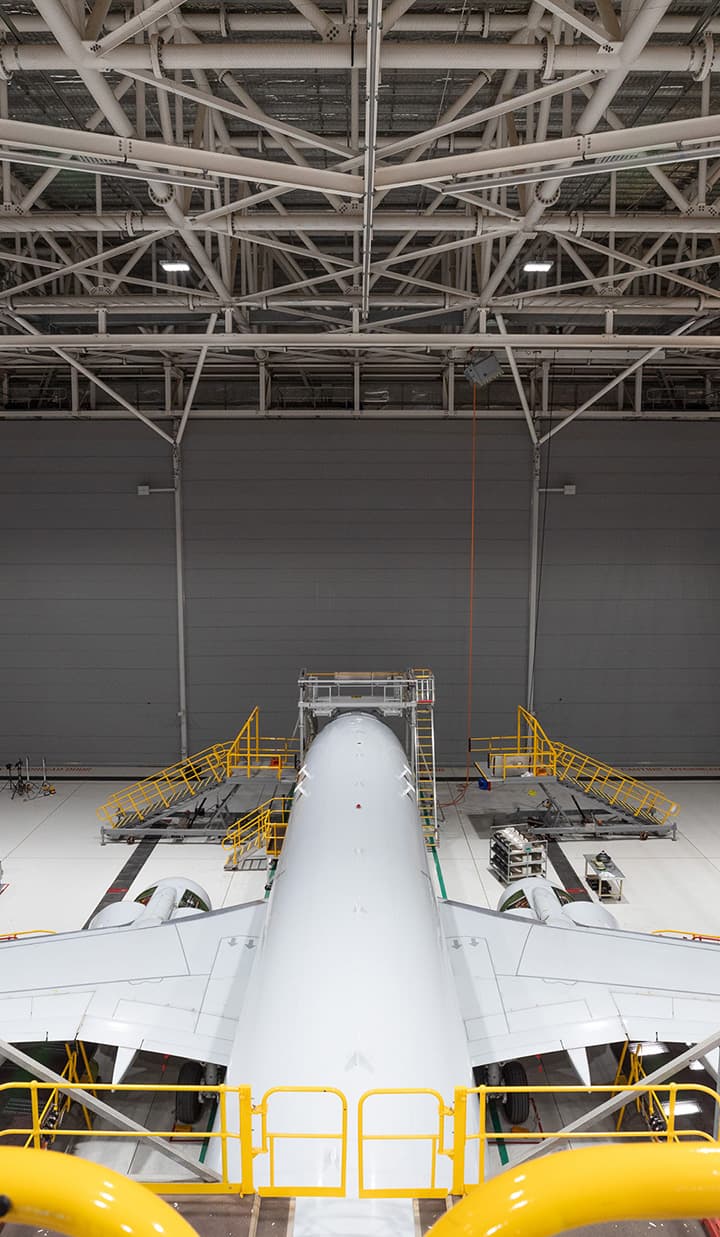 Aircraft in hangar with yellow maintenance platforms.
