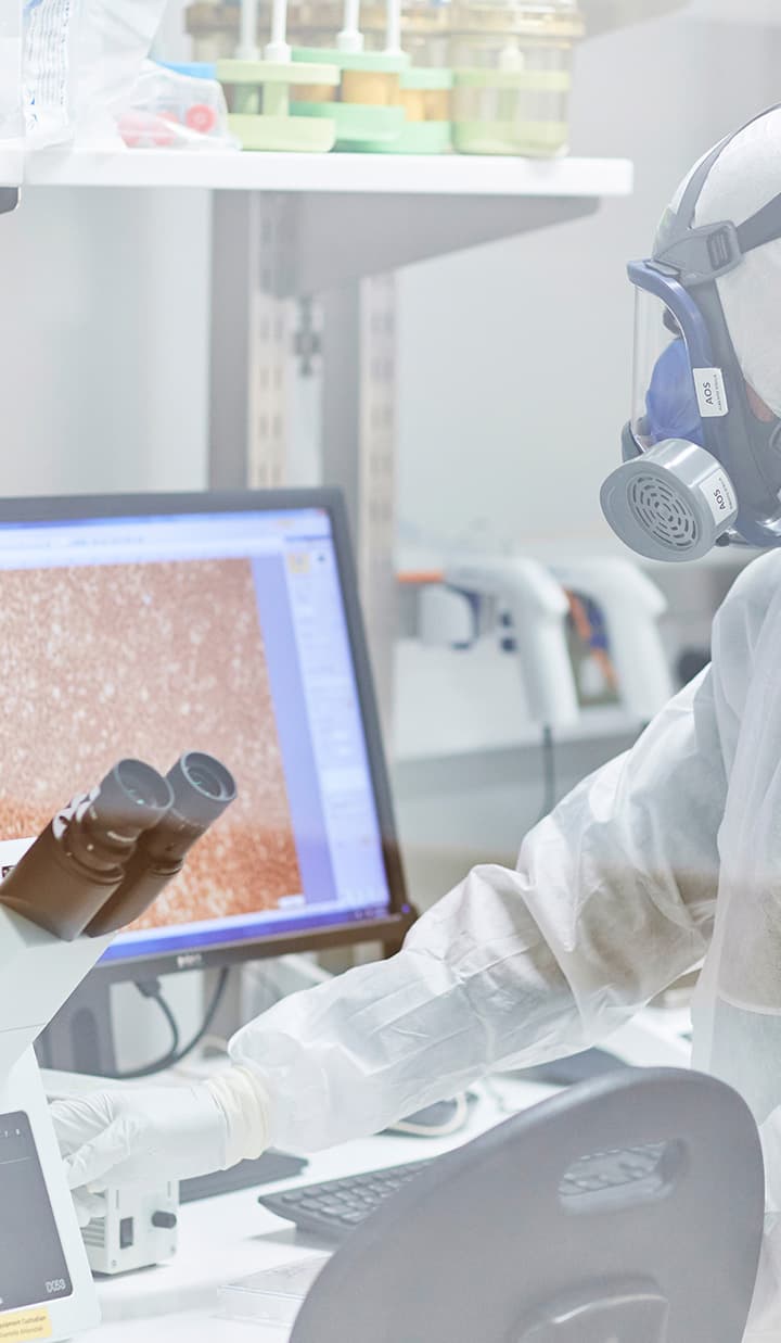 A lab technician wear protective gear while using the microscope.