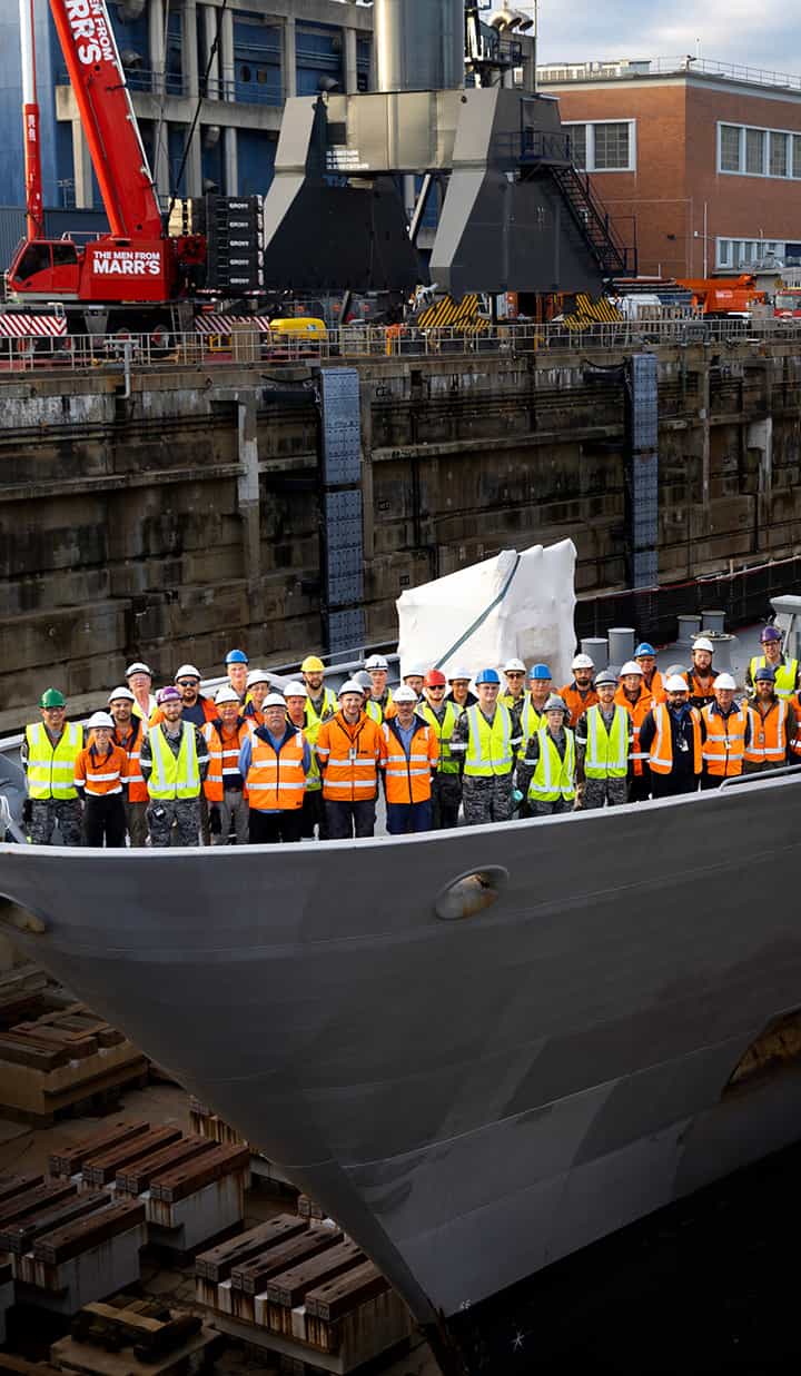 Large group of workers in safety vests standing on ship.