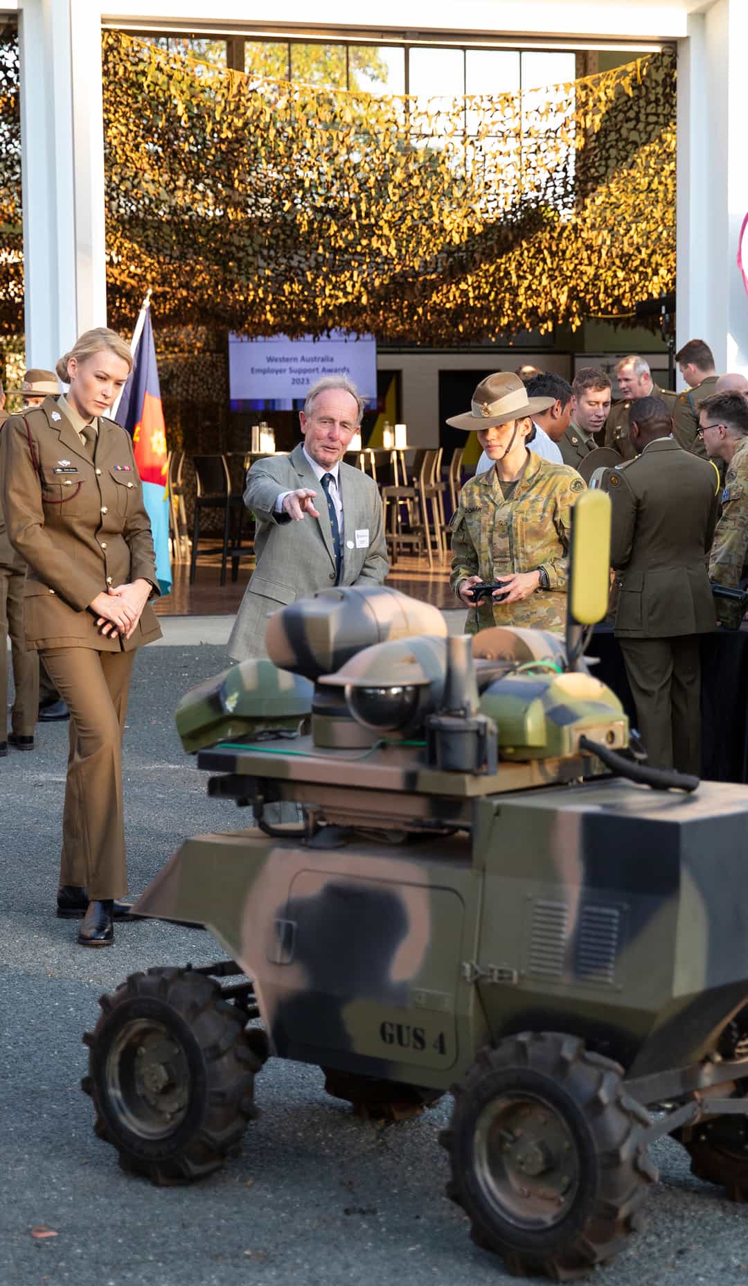 military personnel and officials examining camouflage robotic vehicle