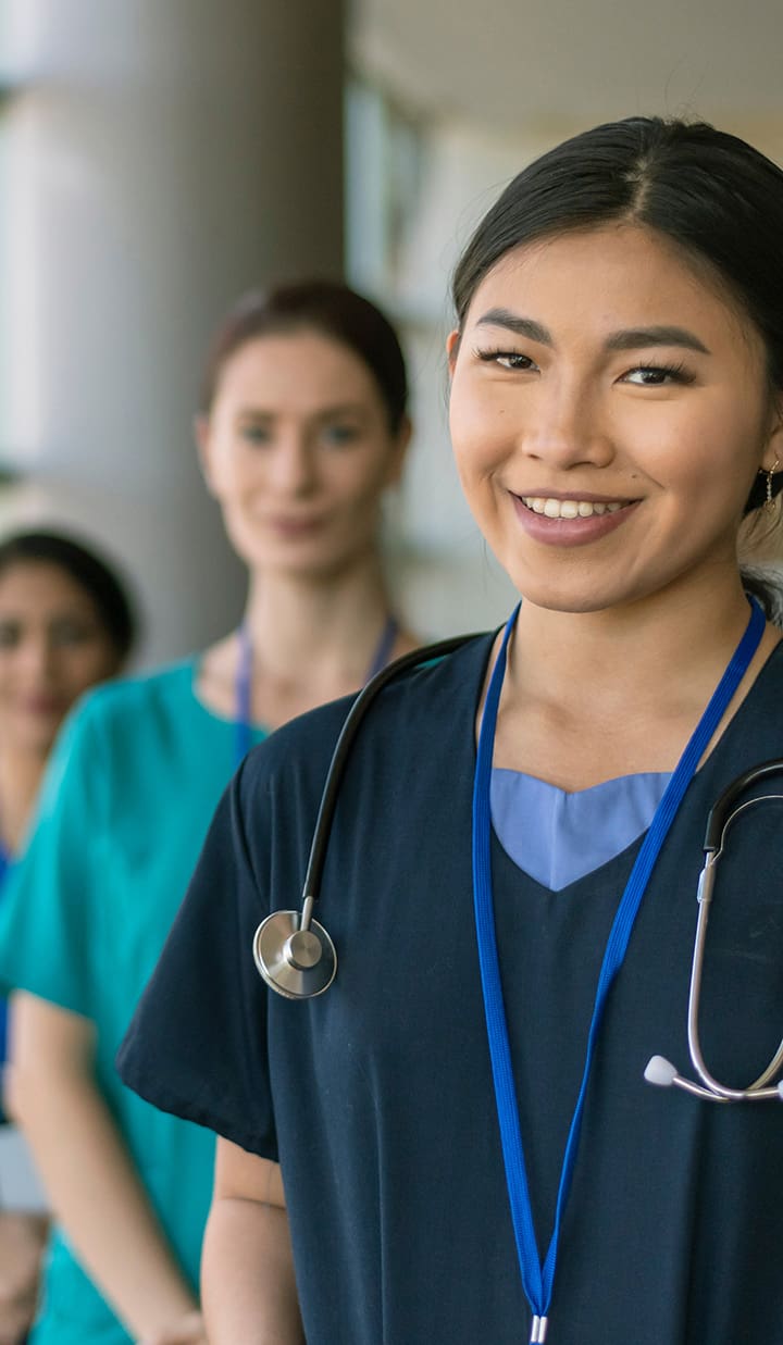 A group of healthcare professionals in scrubs stand in a line in a hospital corridor, with stethoscopes visible on their uniforms.