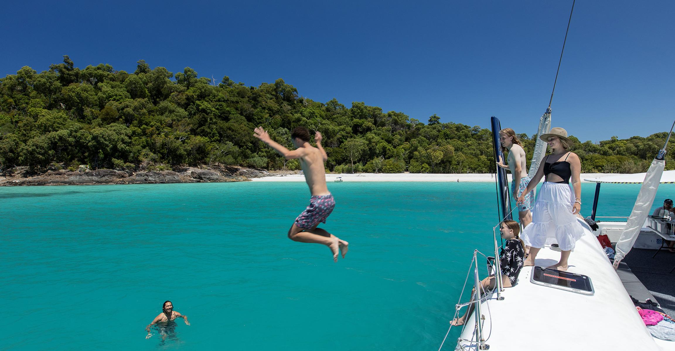People enjoying leisure time, jumping off a boat into crystal clear blue water
