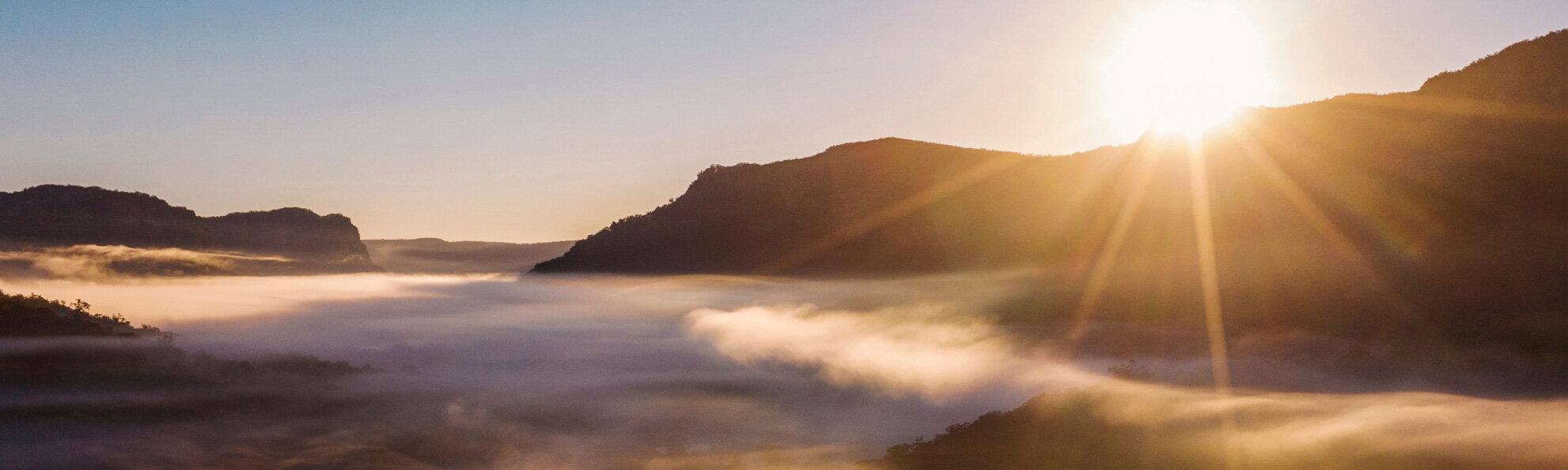 the sun rising over a foggy valley