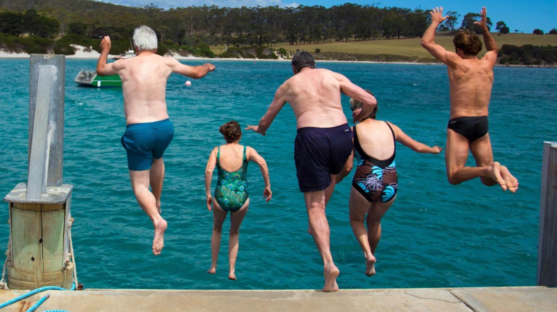 a group of swimmers jumping off a pier